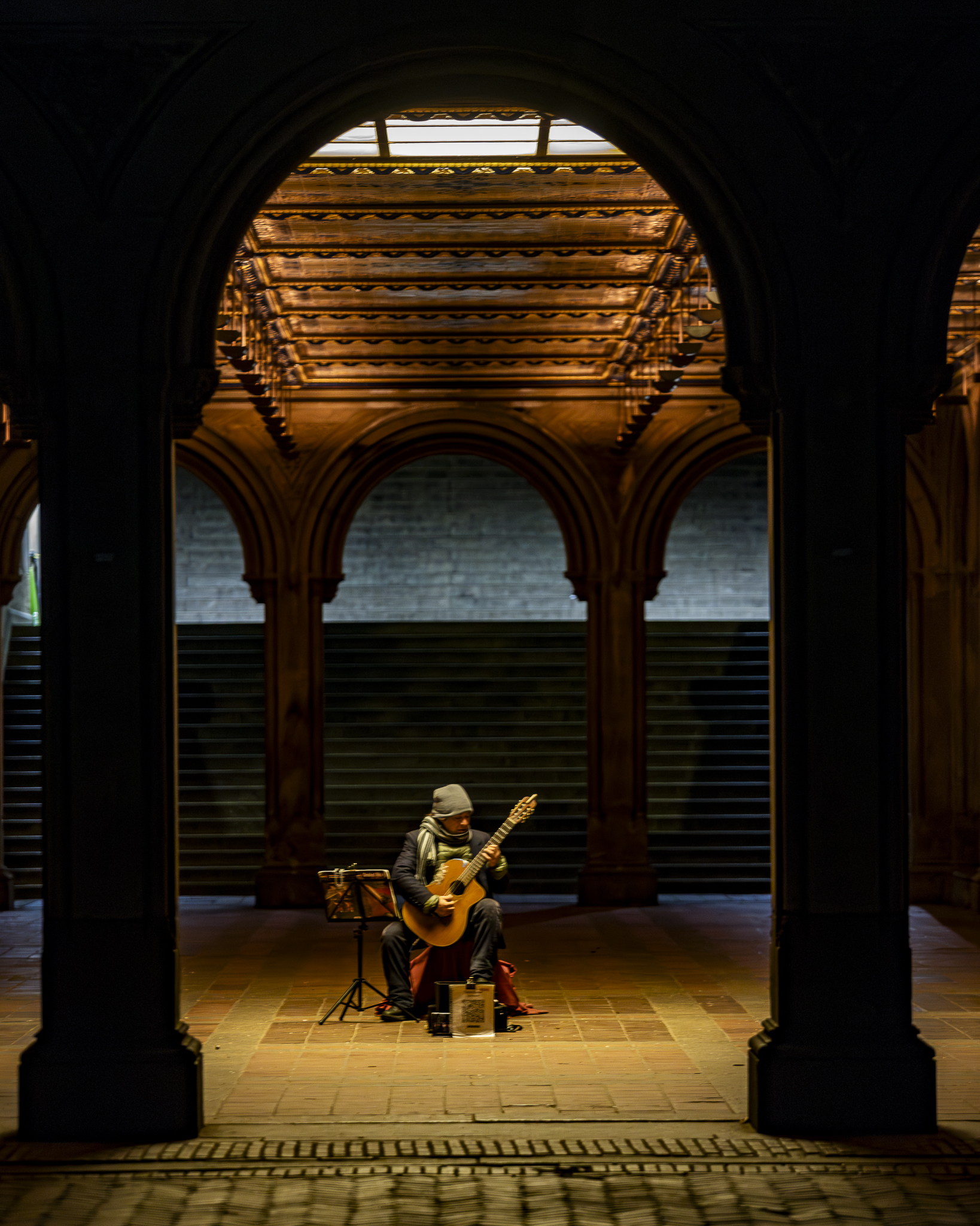 Vertical photo of a guitarist performing beneath the arches at Bethesda Terrace.