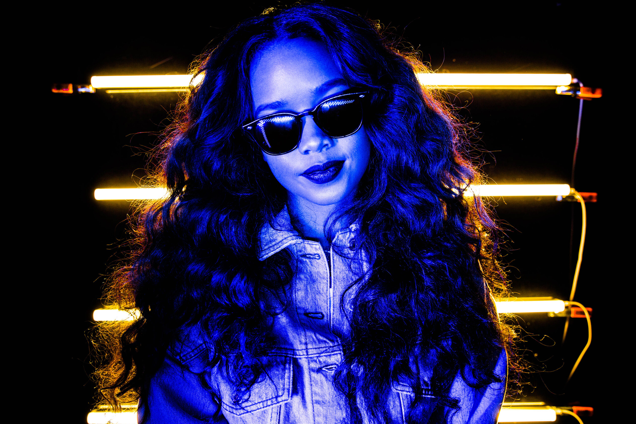 H.E.R. portrait with neon lighting and stylized look in creative studio environment photographed by Ebis Hernandez